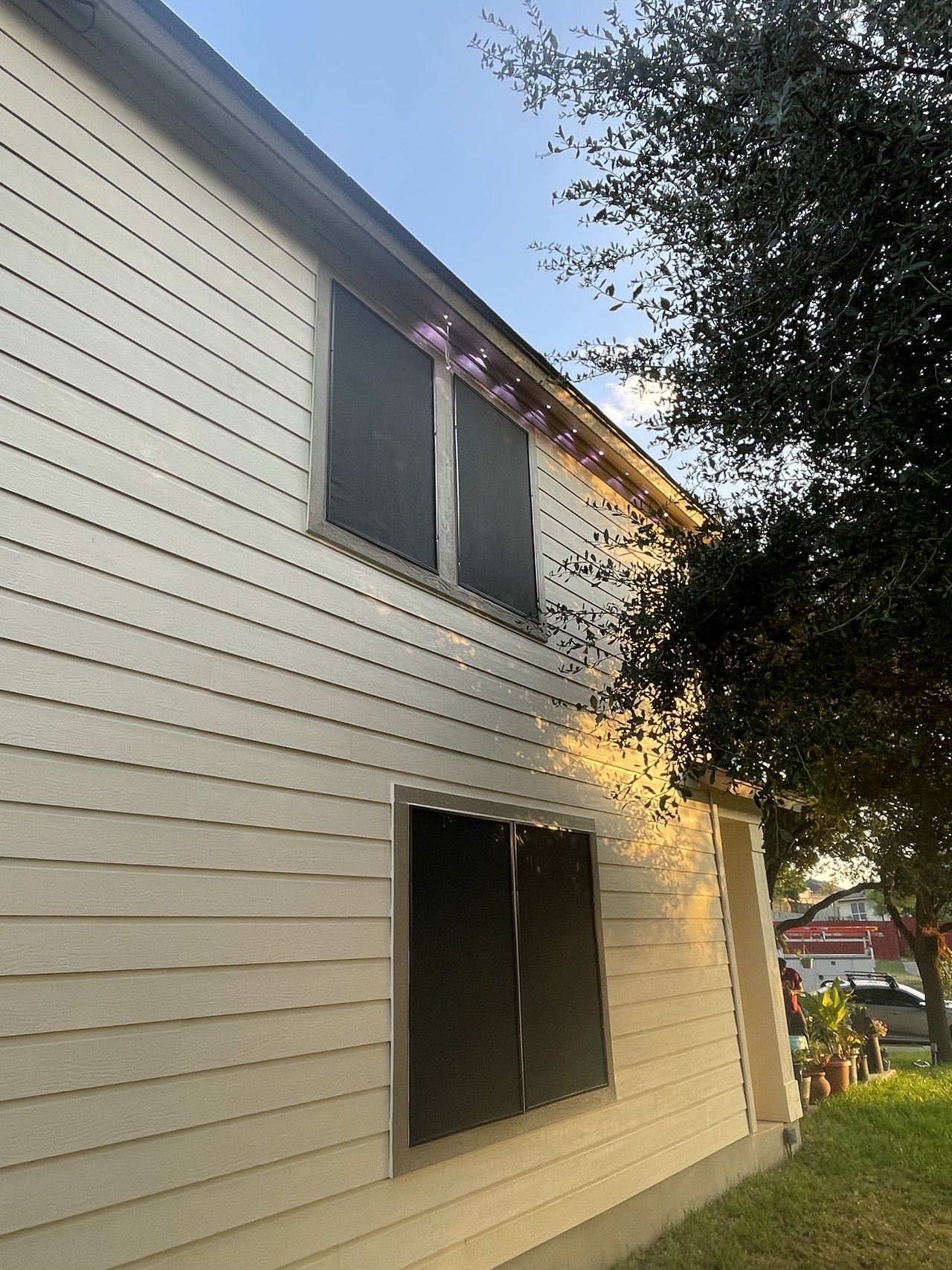 Side view of beige two-story home with solar screens on siding, golden hour lighting