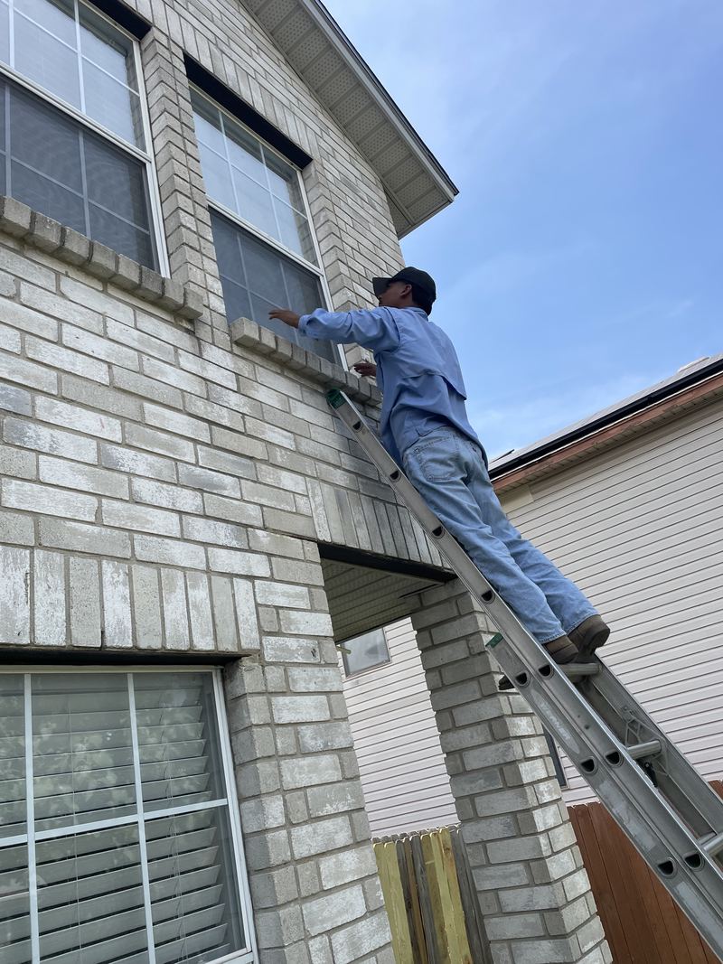 M&J Solar Screens owner on a ladder fitting a mosquito screen to a second-story window